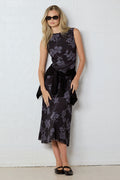 Woman wearing a black floral dress against a white wall