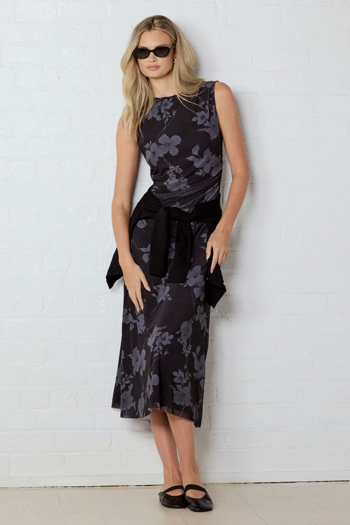 Woman wearing a black floral dress against a white wall