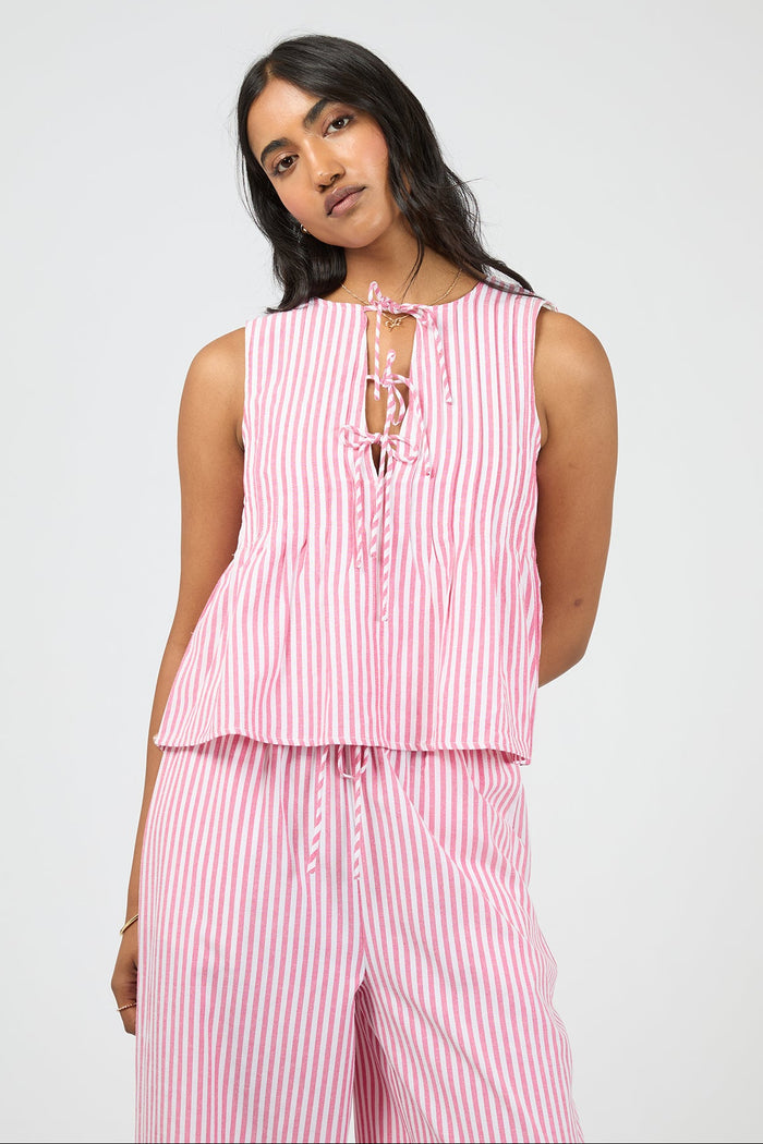 Woman wearing a pink and white striped sleeveless top and pants on a light gray background
