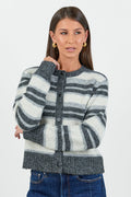 A woman wearing a striped knit cardigan in shades of grey and white with a button-down front, paired with dark blue high-waisted jeans.