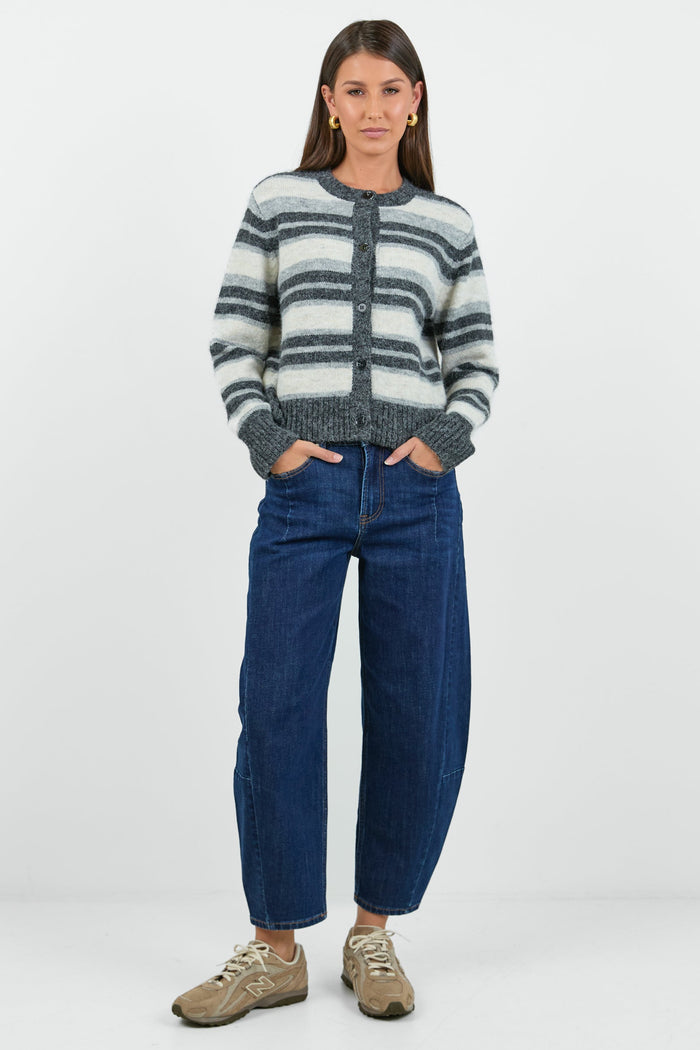A woman wearing a striped knit cardigan in shades of grey and white with a button-down front, paired with dark blue high-waisted jeans.