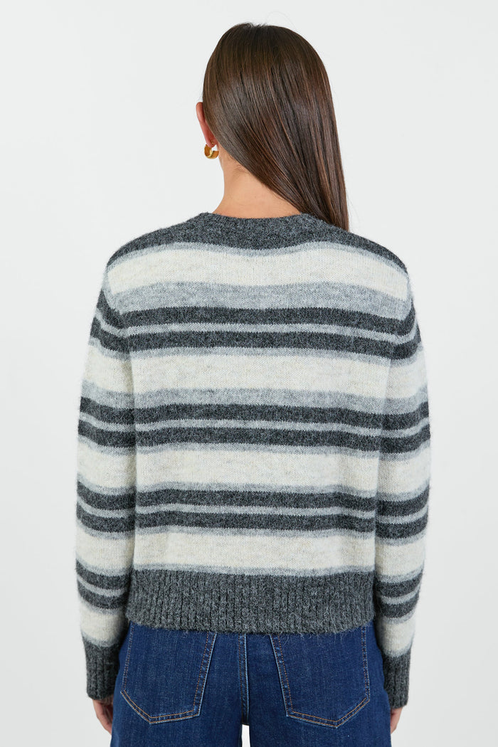 A woman wearing a striped knit cardigan in shades of grey and white with a button-down front, paired with dark blue high-waisted jeans.