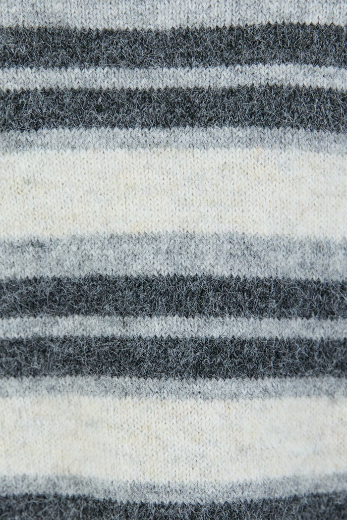 A woman wearing a striped knit cardigan in shades of grey and white with a button-down front, paired with dark blue high-waisted jeans.