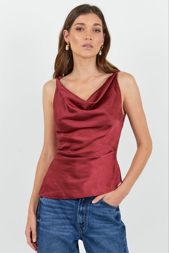 Woman wearing a red cowl neck top and dark blue jeans on a white background.