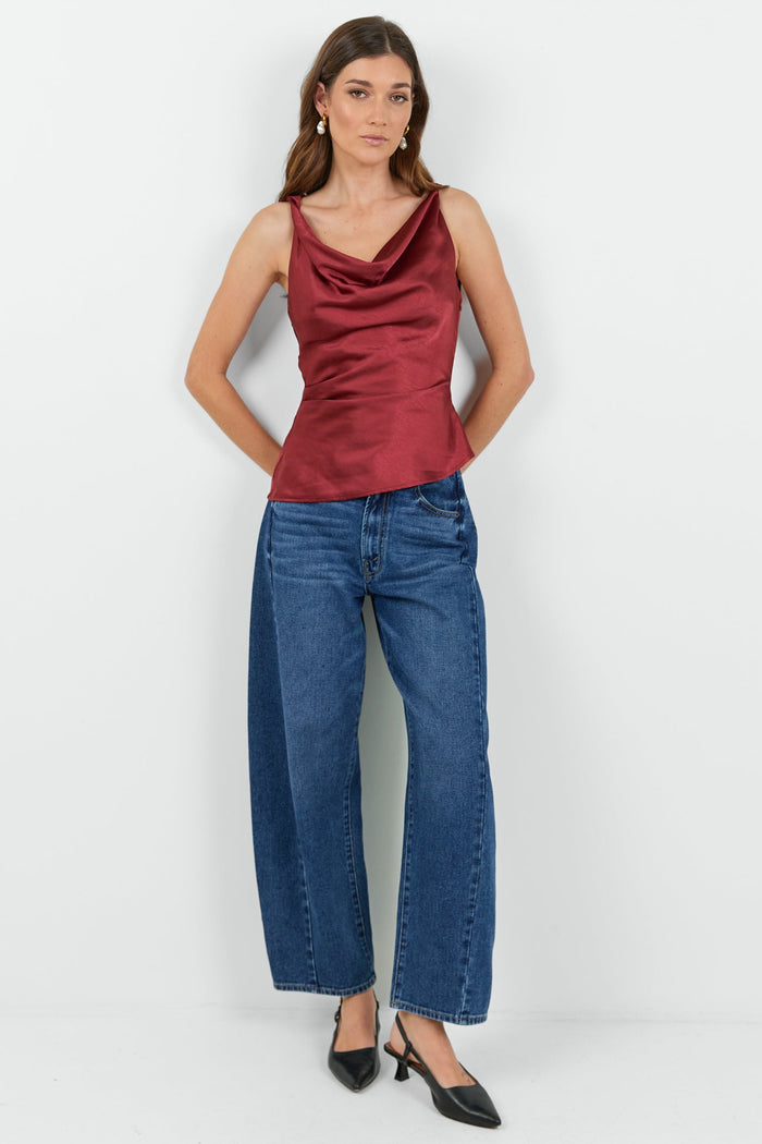 Woman wearing a red cowl neck top and dark blue jeans on a white background.