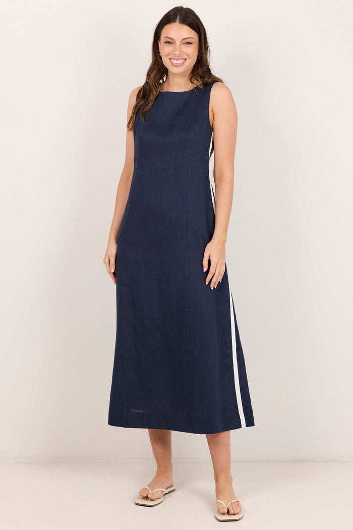 A woman modeling a sleeveless navy midi dress with white side stripes, standing against a plain off-white studio background.