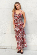 Woman in a floral dress standing against a light gray wall.
