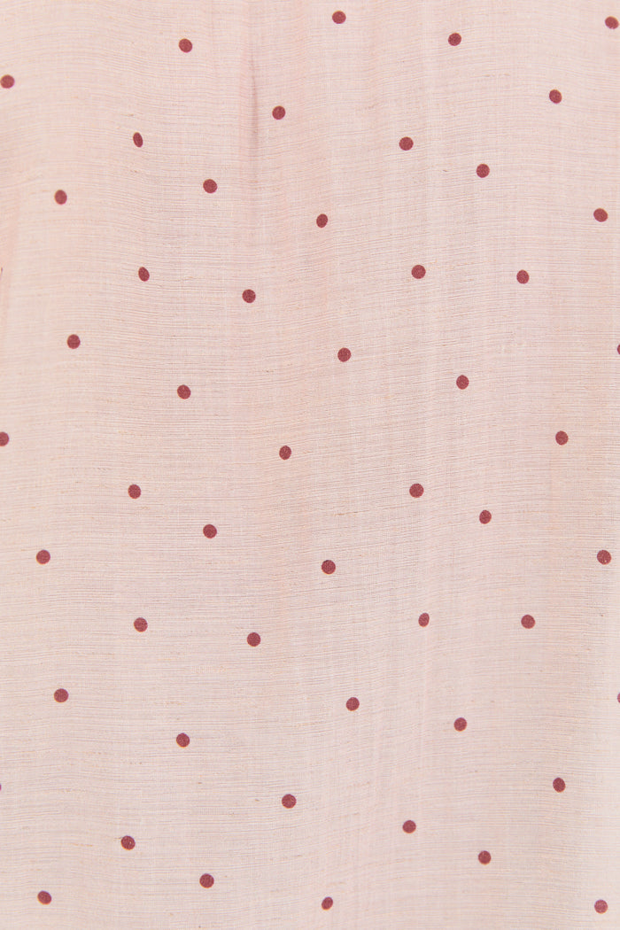 A close-up of a light blush pink fabric with a repeating pattern of small, evenly spaced dark red dots.