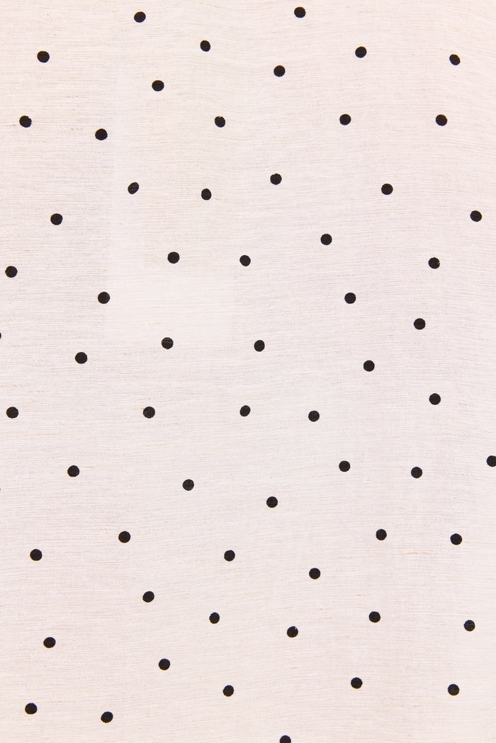 A close-up of a light cream fabric with a scattered pattern of small black polka dots.