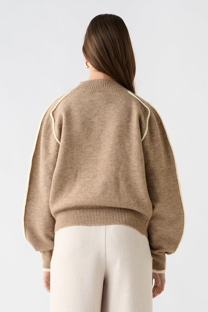 Person wearing a beige sweater and white pants on a white background