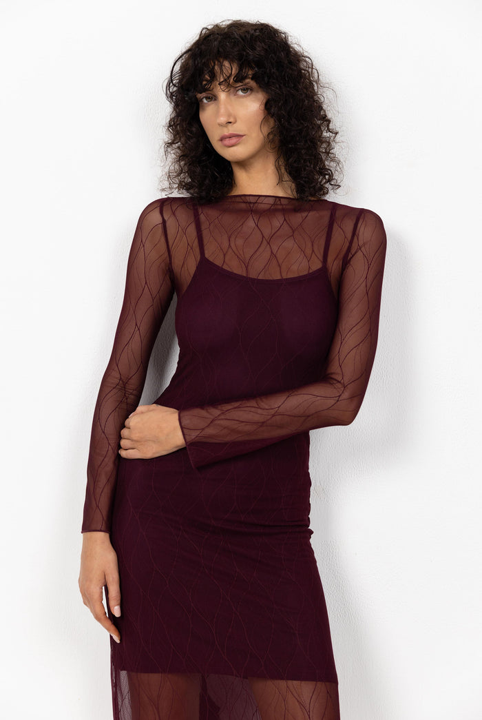Woman wearing a burgundy dress with sheer sleeves against a white background