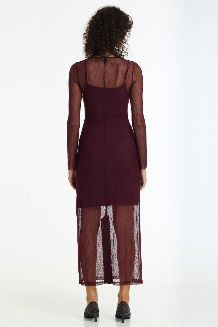 Woman wearing a burgundy dress with sheer overlay on a white background