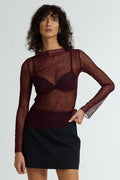 Woman wearing a sheer burgundy top with long sleeves and a black skirt on a white background