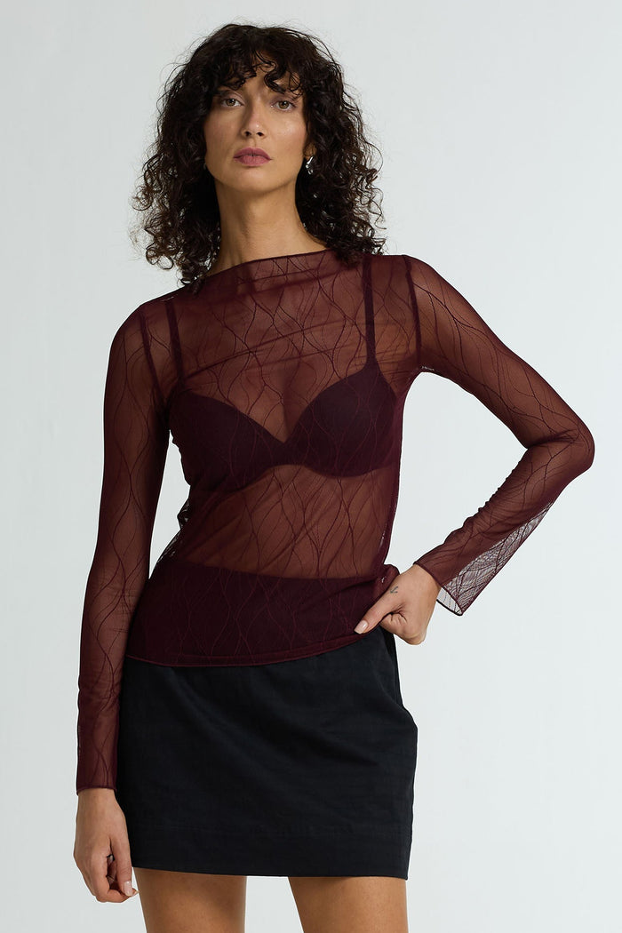 Woman wearing a sheer burgundy top with long sleeves and a black skirt on a white background