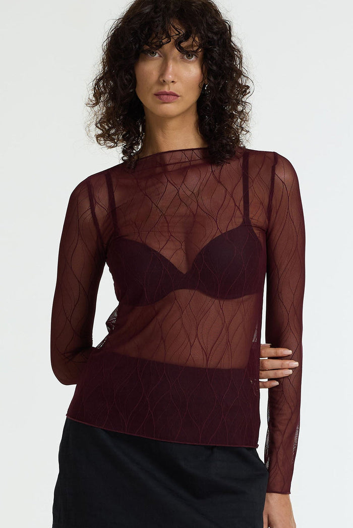 Woman wearing a sheer burgundy top with long sleeves on a white background