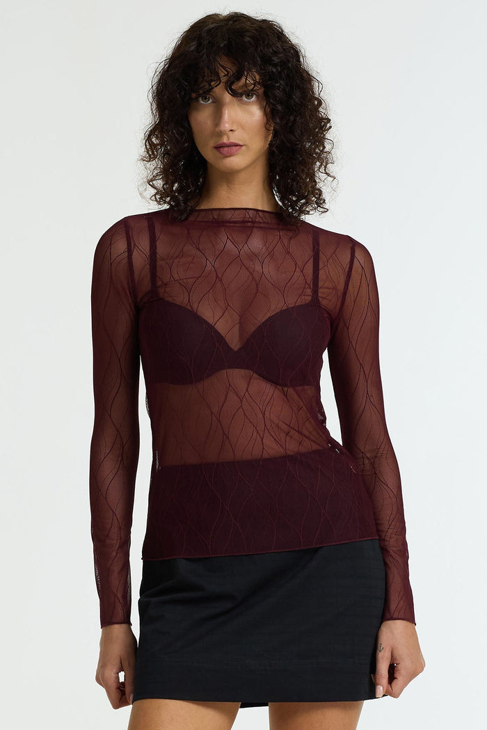 Woman wearing a sheer burgundy top and black skirt on a white background