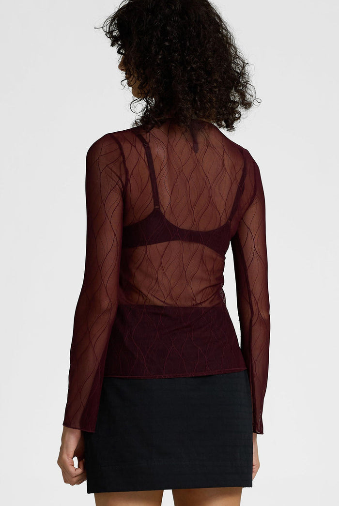 Person wearing a sheer burgundy top with a plain background
