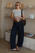 Woman standing in a room with shelves and a counter, holding a drink.