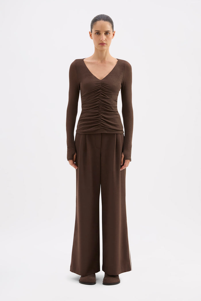 Woman wearing a brown ruched top and wide-leg pants on a white background