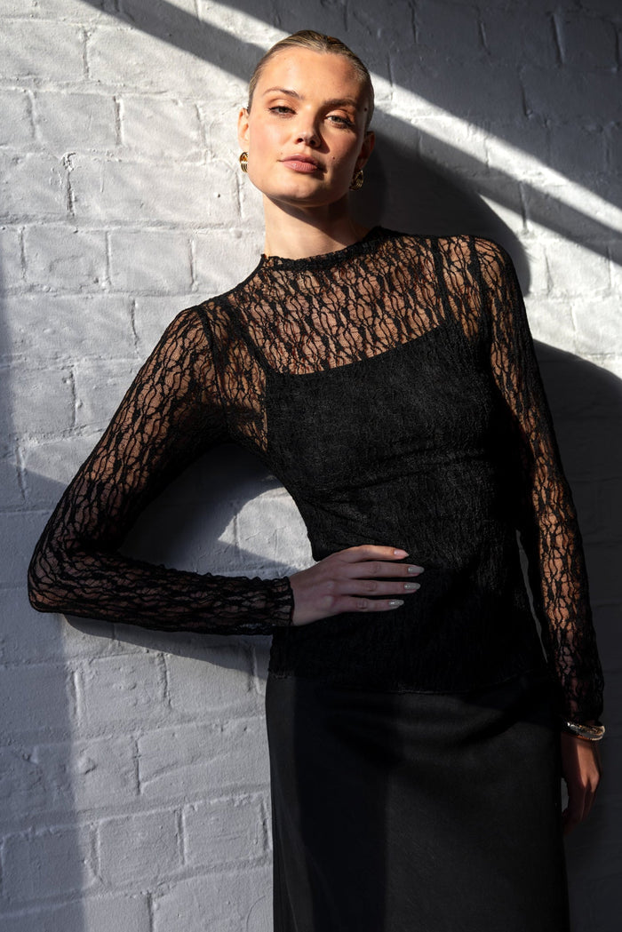 Person wearing a black lace top against a white brick wall