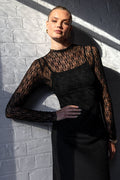 Person wearing a black lace top against a white brick wall