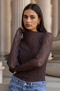 Woman wearing a dark brown sweater and blue jeans standing in front of classical architecture.