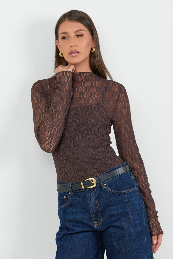A woman wearing a fitted long-sleeve chocolate-brown lace top with a square neckline, paired with dark blue high-waisted jeans.