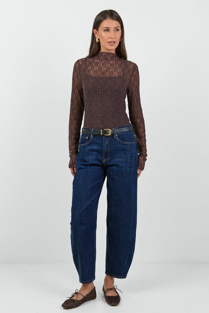 A woman wearing a fitted long-sleeve chocolate-brown lace top with a square neckline, paired with dark blue high-waisted jeans.