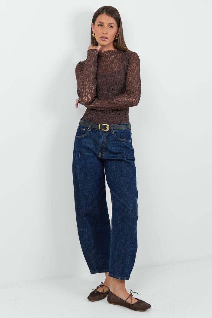 A woman wearing a fitted long-sleeve chocolate-brown lace top with a square neckline, paired with dark blue high-waisted jeans.