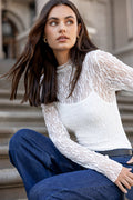 Woman wearing a white lace top and blue jeans sitting on steps.