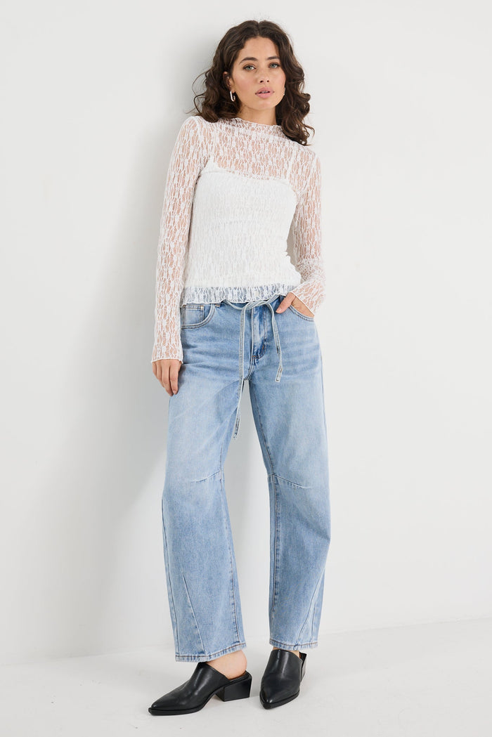 Woman wearing a patterned sweater, white shirt, blue jeans, and black shoes on a white background