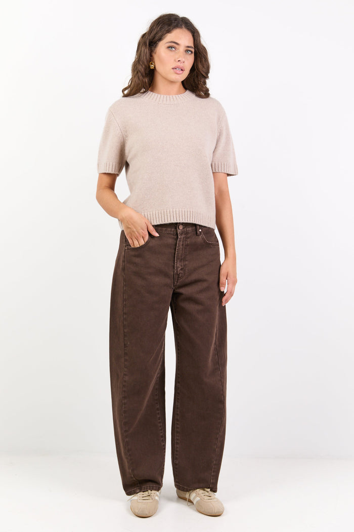 Woman wearing a beige sweater and brown pants on a white background