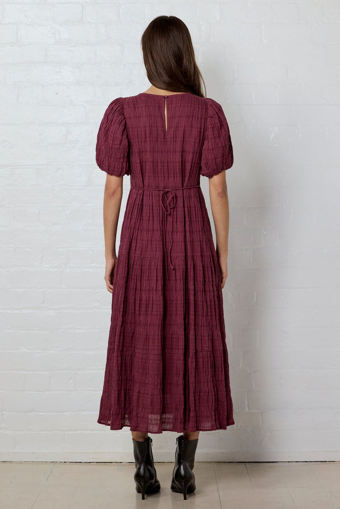 Woman wearing a burgundy dress against a white brick wall.