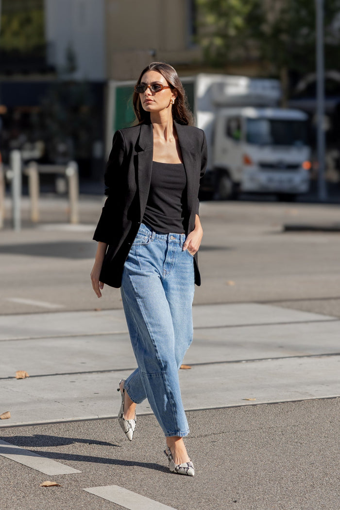 Woman walking on a city street wearing a black blazer, black top, and light blue jeans.