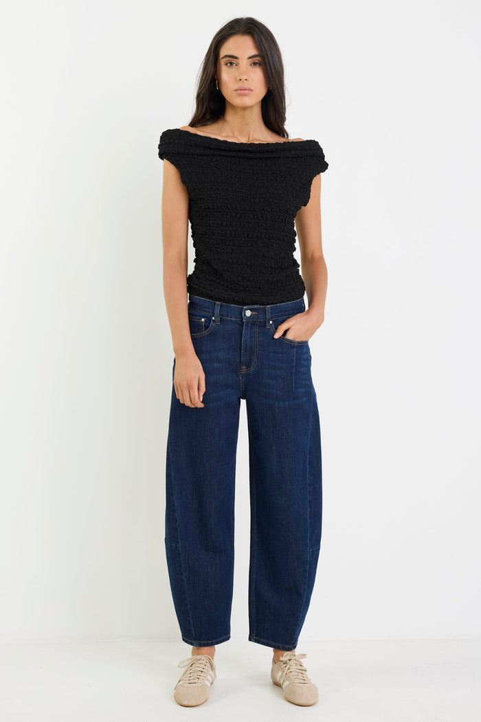 Woman wearing a black off-shoulder top and blue jeans on a white background