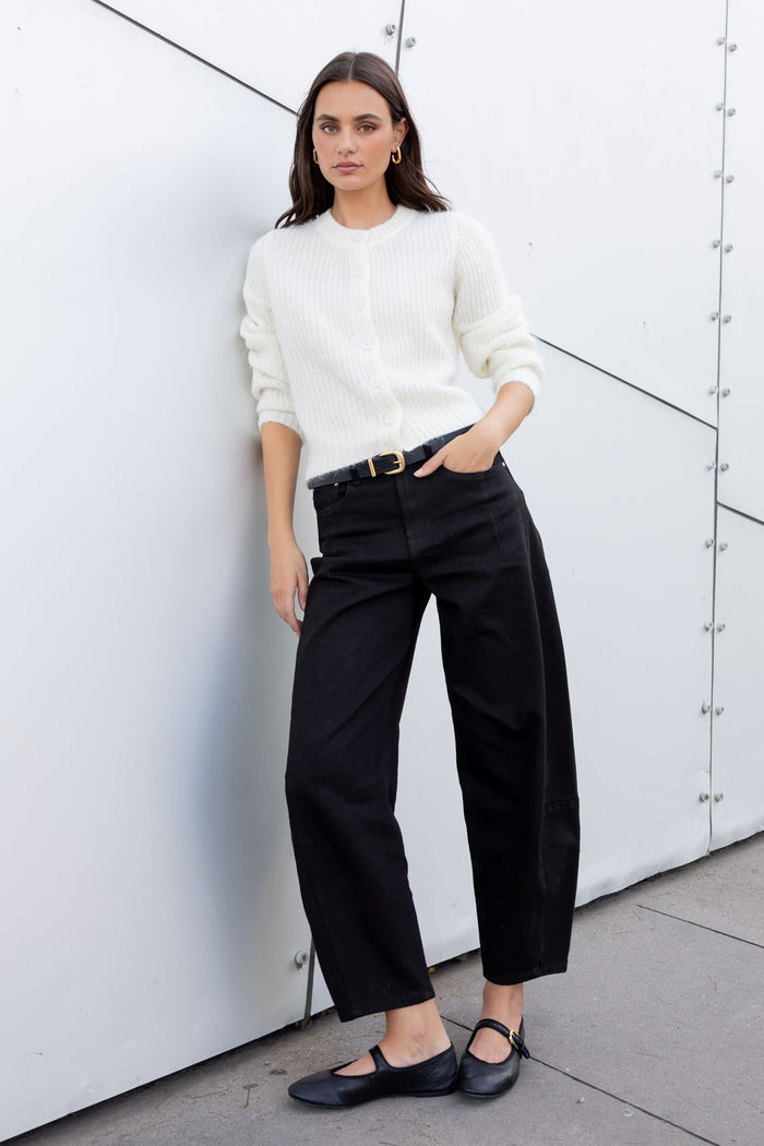 Woman in a white shirt and black pants standing against a modern architectural wall.