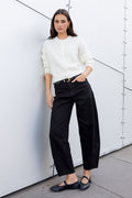 Woman in a white shirt and black pants standing against a modern architectural wall.