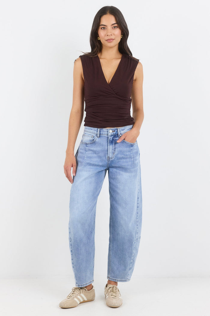 Woman wearing a brown sleeveless top and light blue jeans on a white background