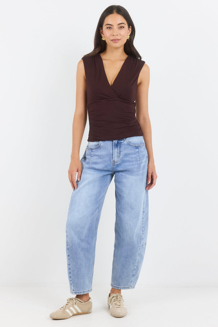 Woman wearing a brown sleeveless top and light blue jeans on a white background