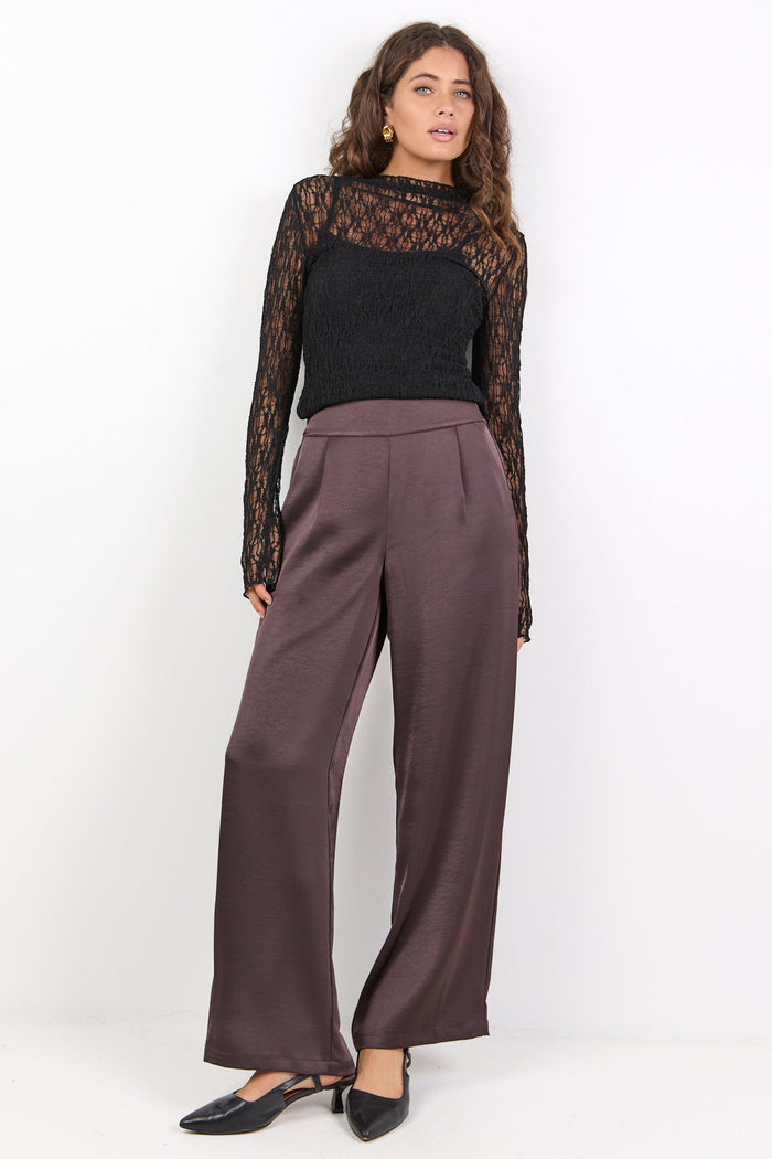Woman wearing a black top and brown pants on a white background