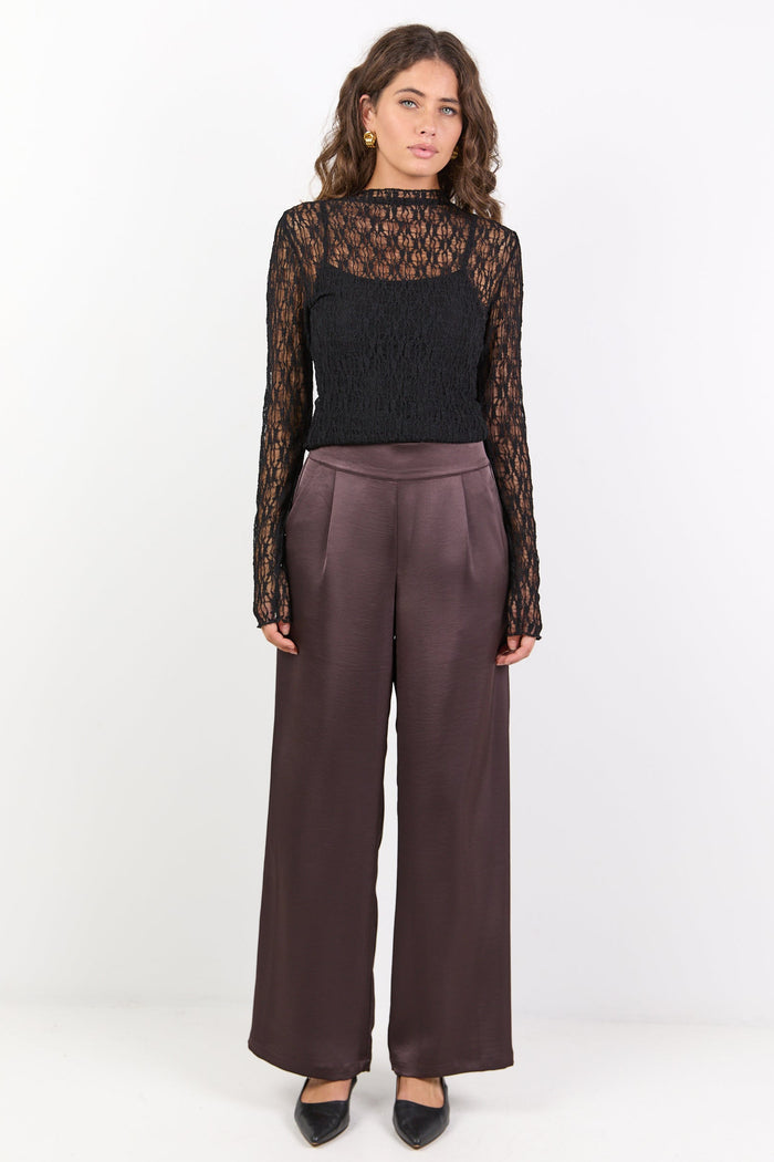 Woman wearing a black lace top and brown pants on a white background