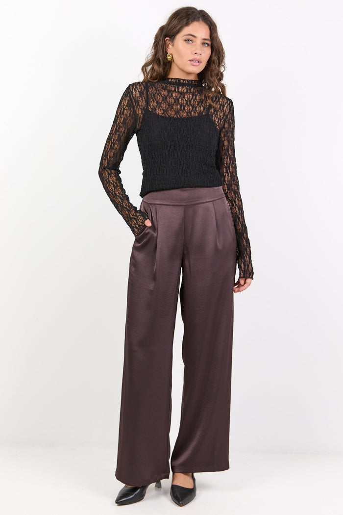 Woman wearing a black lace top and brown pants on a white background