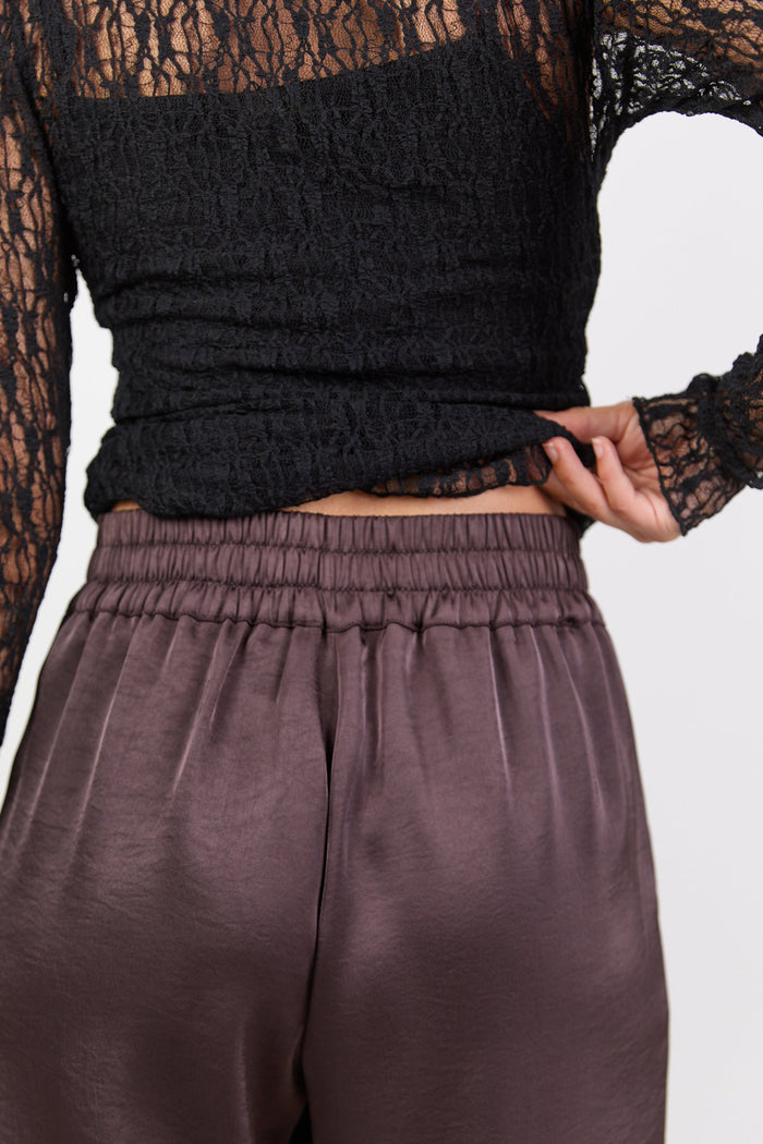 Person wearing a black top with lace details and brown pants on a white background