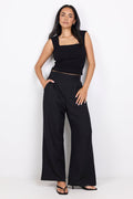 Woman wearing a black sleeveless top and wide-leg pants on a white background