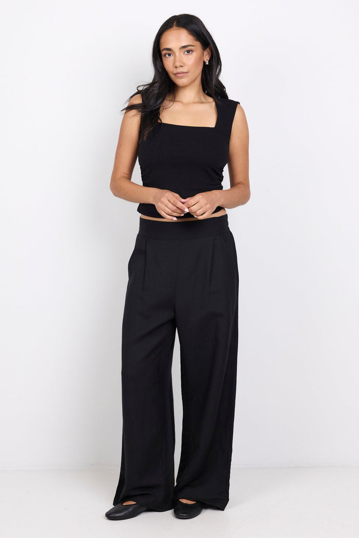 Woman wearing a black sleeveless top and wide-leg pants on a white background