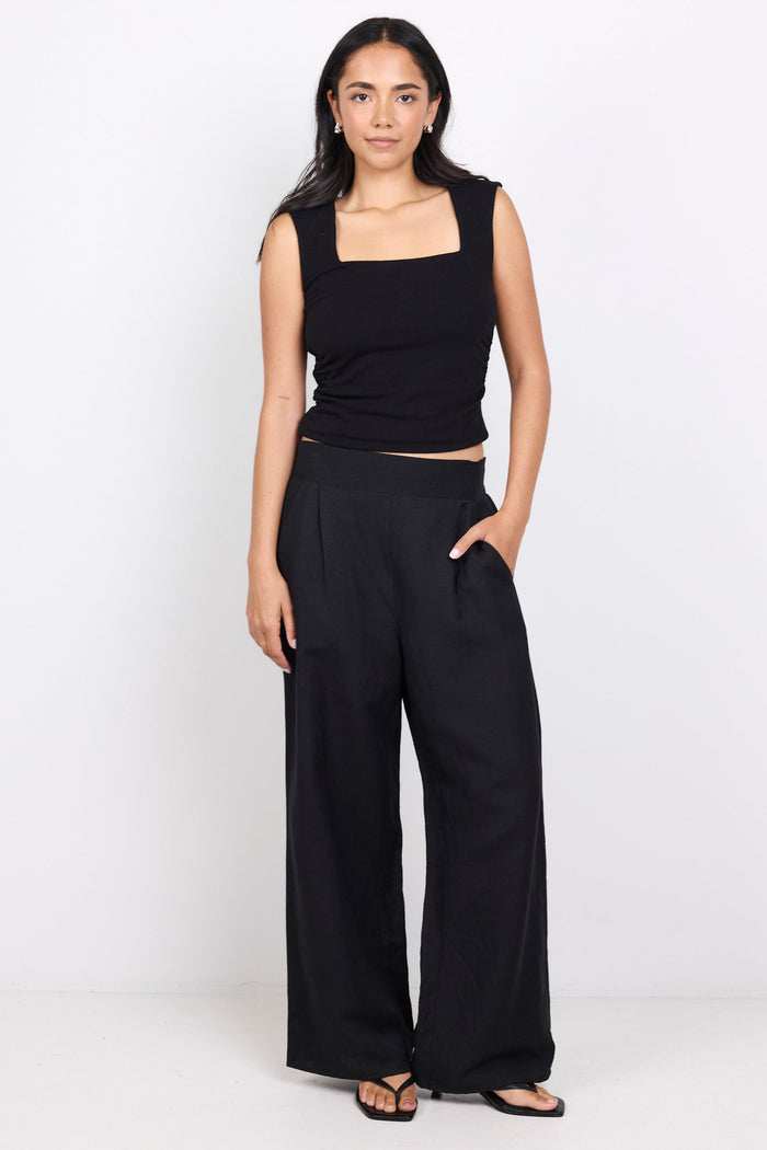 Woman wearing a black sleeveless top and wide-leg pants on a white background