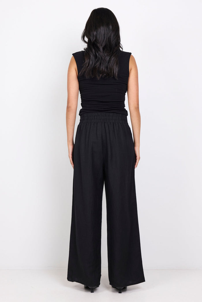 Person wearing a black sleeveless top and wide-leg pants on a white background