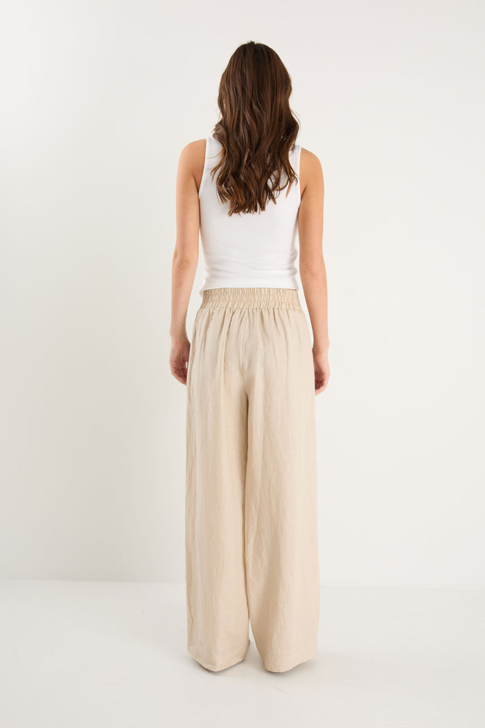 Woman wearing a white sleeveless top and beige wide-leg pants on a white background