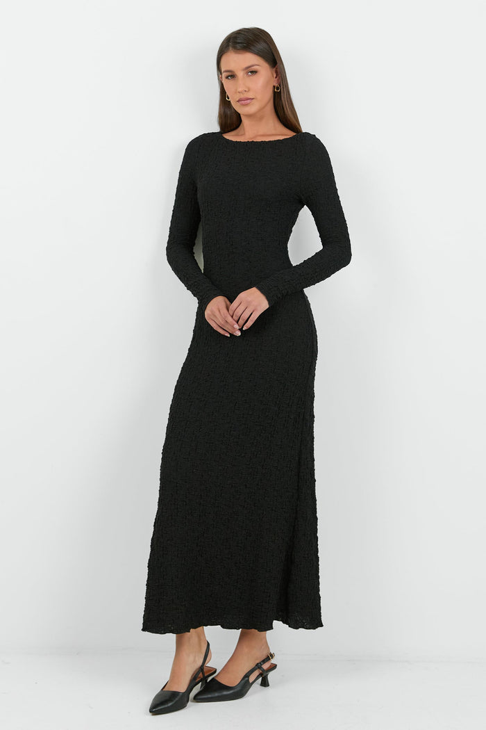 A woman wearing a long-sleeve black textured maxi dress with a fitted silhouette.
