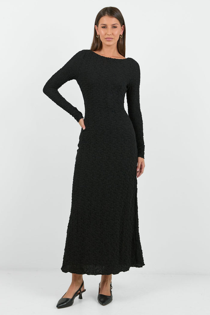 A woman wearing a long-sleeve black textured maxi dress with a fitted silhouette.